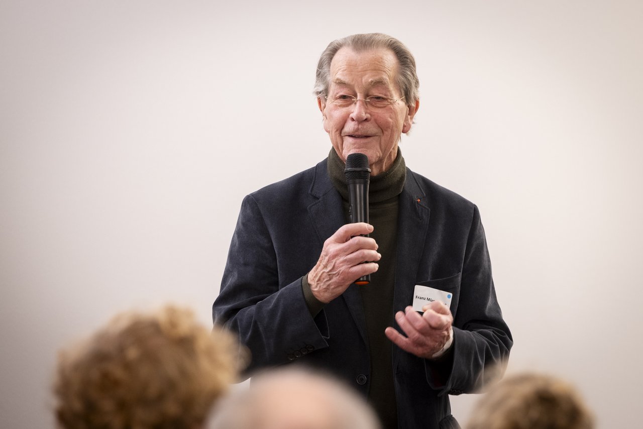 Ein alter Mann, Franz Müntefering, steht vor Publikum und spricht in ein Mikrofon. Er trägt ein dunkles Jackett und darunter eine dunkelbraunen Rollkragenpullover. Klick öffnet eine vergrößerte Ansicht.