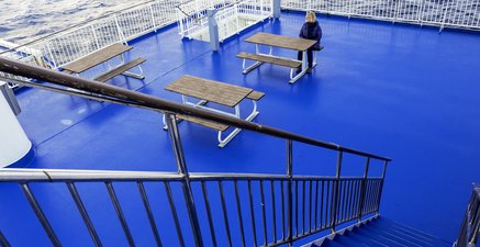 Auf einem Schiff ganz in Blau führt eine Treppe hinunter aufs Deck zu einer Frau alleine am Tisch.
