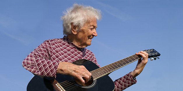 Eine alte Frau spielt draußen auf einer Gitarre