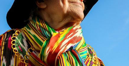 Ältere Frau in bunter Kleidung mit Hut vor blauem Himmel