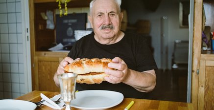 Älterer Mann Rollstuhl sitzt am Tisch und hält zwei traditionell jüdische Brotzöpfe in den Händen.