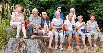 Eine Gruppe Senioren ruht sich während eines gemeinsamen Spaziergangs auf einer Bank aus