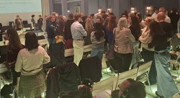 Blick in den Saal. Die meisten Personen stehen beieinander und unterhalten sich.