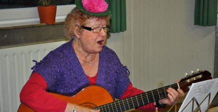 Ältere Frau in lustiger Verkleidung spielt Gitarre und singt dazu