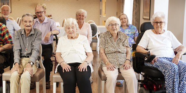 Eine Gruppe älterer Menschen in zwei Reihen sitzend, lächeln in die Karmera.