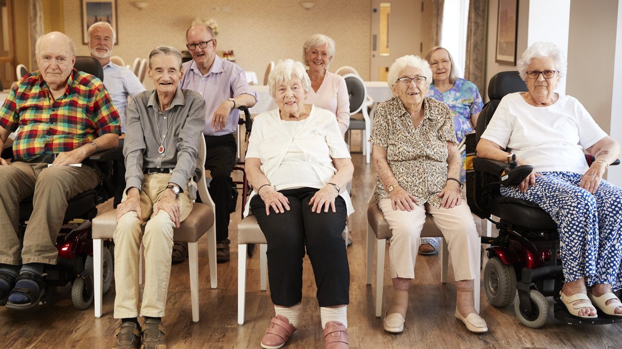 ©Monkey_adobe.stock.com Eine Gruppe älterer Menschen in zwei Reihen sitzend, lächeln in die Karmera.