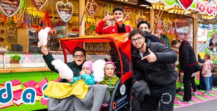 Ein Urgroßvater und zwei Mädchen teilen Zuckerwatte und Lachen in einer Rikscha auf einem lebhaften Jahrmarkt.