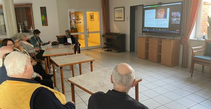 Eine Gruppe von Senior/innen quizzt gemeinsam mit digital zugeschalteten Personen auf Fernseher