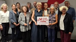 Eine Gruppe von Männern und Frauen stehen vor einer Fotowand der BAGSO. Zwei Frauen halten ein Schild mit der Aufschrift "JA zum Alter" in der Hand.