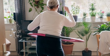 Ältere Frau beim Hullern in ihrem Wohnzimmer  - Ansicht von hinten mit Blick ins Wohnzimmer