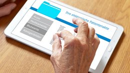 Ein Tablet auf dem die elektronische Patientenakte abgebildet ist. Eine alte Hand ist am Bildschirm aktiv.