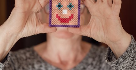 Ältere Frau hält einen bunten Plastikperlenuntersetzer mit Smiley vor ihr Gesicht 
