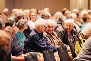 Ein Blick in ein bunt gemischtes Publikum: Im Mittelpunkt zwei ältere Männer und eine ältere Frau, die miteinander lachen.