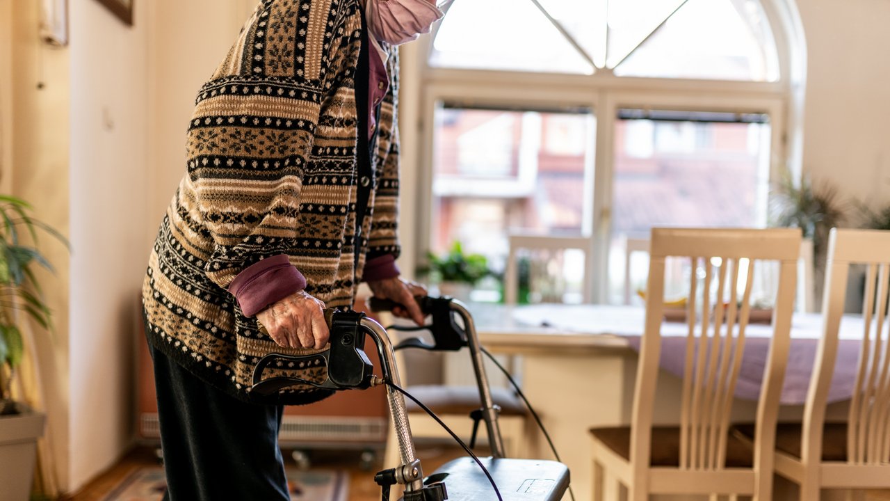 Alte Frau geht mit dem Rollator durch die Wohnung.