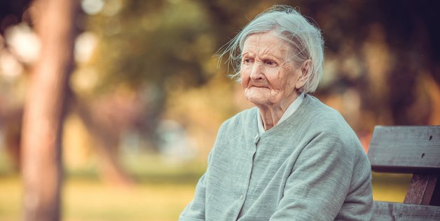 Eine alte Frau sitzt auf einer Bank im Park. Sie schaut sehr traurig
