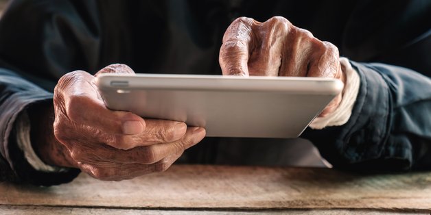 Ein alter Mann hält ein tablet in den Händen