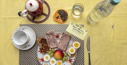 Gedeckter Frühstückstisch mit Wasserflasche und Zettel "Bitte austrinken"