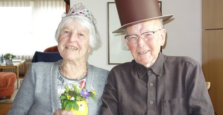 Ein altes Ehepaar am 66. Hochzeitstag. sitzt nebeneinander und lacht. Sie hat eine Krone und er einen Zylinder auf dem Kopf. 