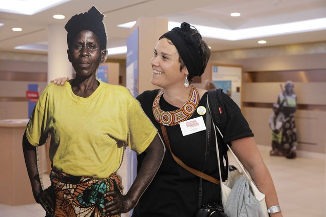 A woman smiling at an actual-sized cardboard stand-up of an African woman.