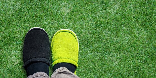 Füße mit grünem und schwarzem Pantoffel von oben auf einer Wiese.