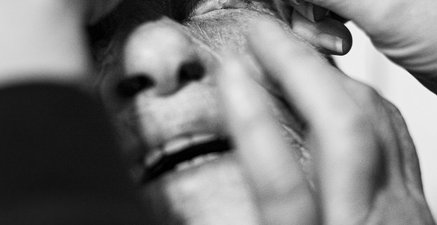 Schwarz-Weiß Foto, eine alte Dame bekommt mit einer kleinen Pipette die Augen getropft