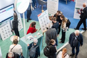 Der Blick von oben, auf einen Messestand. Einige Personen halten sich darin auf.