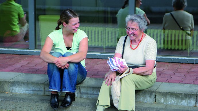 Junge und ältere Frau sitzen auf einer Treppenstufe und unterhalten sich.