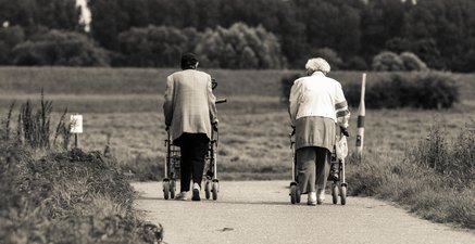 Zwei Seniorinnen mit Rolatoren am Rhein-Deich, nebeneinander von hinten fotografiert