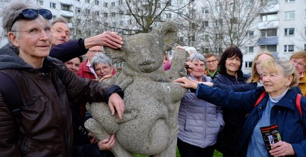 Eine altersgemischte Personengruppe steht um einen Stein-Koala herum.