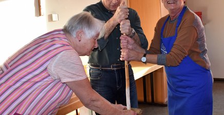Zwei Frauen und ein Mann stehen am Butterfaß und wollen die Sahne zu Butter verarbeiten.  Es macht Spaß.