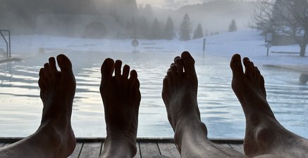 Füße und Panorama. Rentnerpaar in einer Sauna mit Blick auf eine verschneite Berglandschaft. 