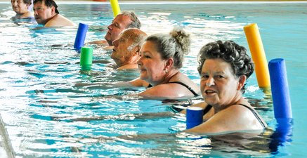 Gruppe von Menschen unterschiedlichen Alters in einem Schwimmbecken mit Schwimmnudeln