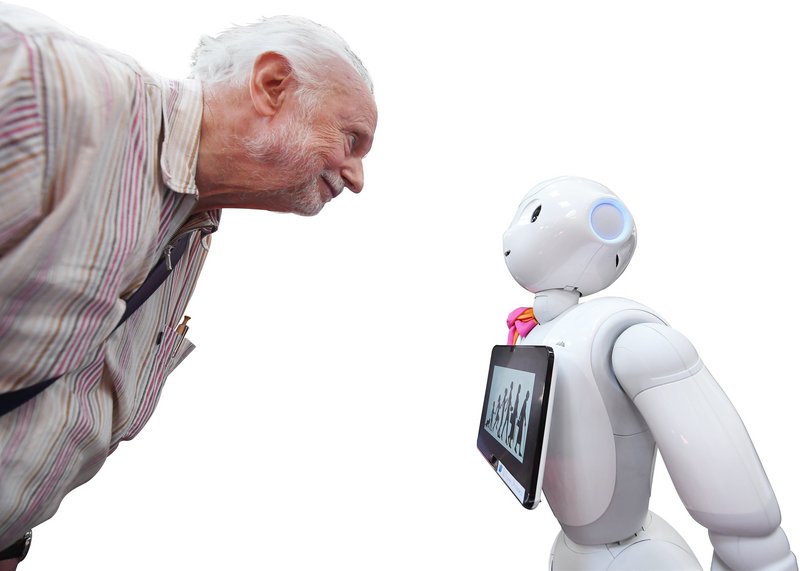 Ein alter Mann steht vor einem kleinen Roboter und schaut lächelnd zu ihm runter.