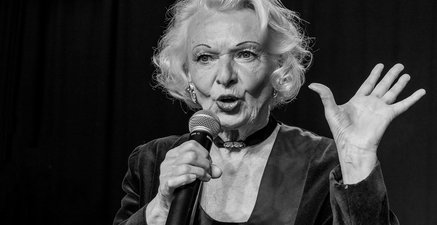 Ältere Frau, die Marlene Dietrich ähnelt, singt mit Mikrofon auf einer Bühne