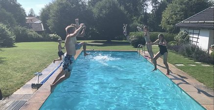 Ältere Frau und viele Kinder springen gleichzeitig in einen Swimming-Pool.