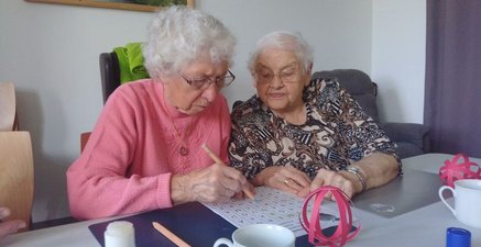 Auf dem Bild helfen sich zwei ältere Damen bei einem Gitterkreuzworträtsel