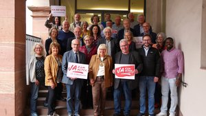 Eine Gruppe von Menschen steht auf einer Treppe. Einige von ihnen halten ein Schild mit dem Aufdruck "Ja zum Alter!" in der Hand.