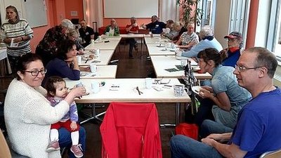 An Tischen, die im Kreis aufgebaut sind, sitzen verschiedene junge und alte Menschen. Sie haben Der Tisch ist für eine Mahlzeit gedeckt. Die Menschen unterhalten sich. 