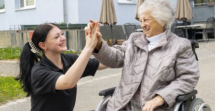 Seniorin im Rollstuhl gibt junger Frau aus dem FSJ-Programm die Hand