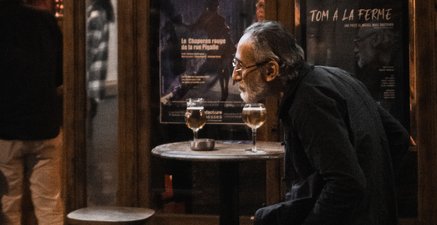 Auf dem Bild setzt sich gerade ein alter Mann auf einen Barhocker vor einer französischen Bar.