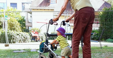 Eine hochaltrige Frau und ein einjähriges Kind am Rollator im Garten einer stationären Pflegeeinrichtung