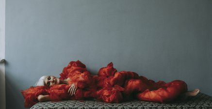 Eine Frau liegt mit geschlossenen Augen in einem roten Kleid auf einem Daybed und träumt ihren Gedanken nach