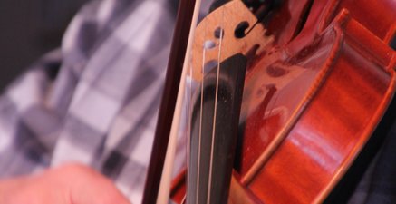 Älterer Mann im karierten Freizeithemd streicht den Bogen über eine Violine
