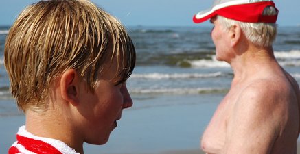 Enkel und Großvater stehen einander zugewandt am Meer, sehen aber in unterschiedliche Richtungen.