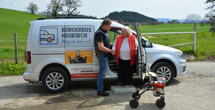 Mann hilft älterer Frau mit Rollator beim Einstieg in den Bürgerbus.