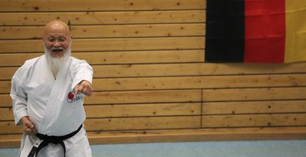 Hideo Ochi (83),ehemaliger Karate Bundestrainer., beim Training. Hinter ihm hängt eine Deutschlandfahne an der Wand.