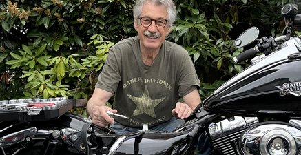 Ergrauter Motorradfahrer schraubt an seiner Harley. Er sieht glücklich aus. 