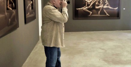 Ein alter Mann steht mit einer gezückten Fotokamera im Ausstellungsraum einer Galerie