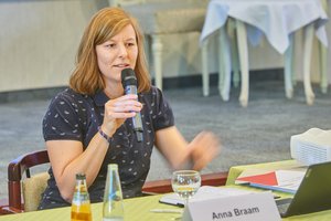 Eine Frau mittleren Alters sitzt an einem Tisch und spricht in ein Mikrofon.