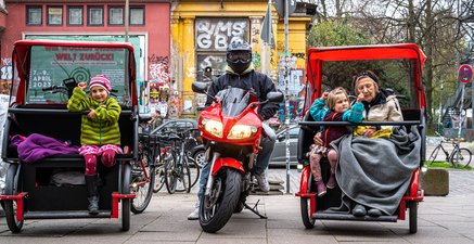 Seniorin in Rikscha behält ihr Tempo bei, während ein rotes Motorrad vorbeisaust.